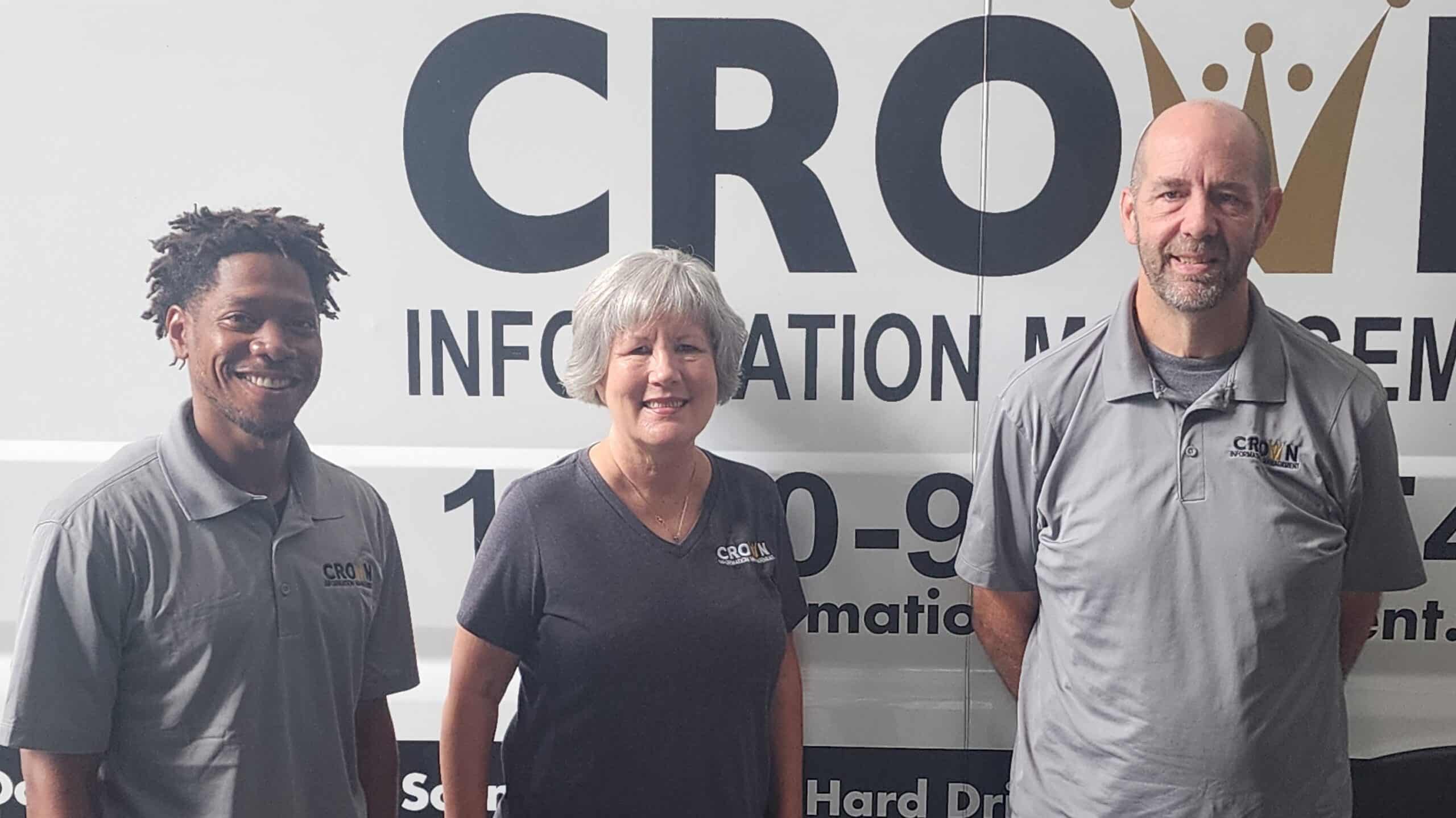 Crown team members smiling for a photo in front of a Crown Information Management vehicle
